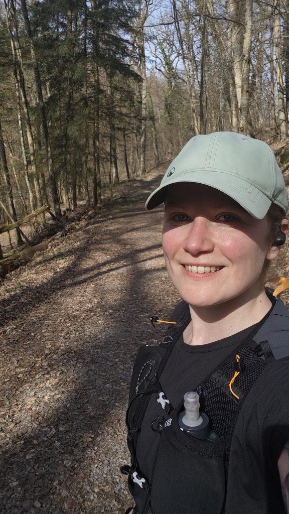 Eine Frau in einem Wald. Sie trägt Laufkleidung und ein Cap.