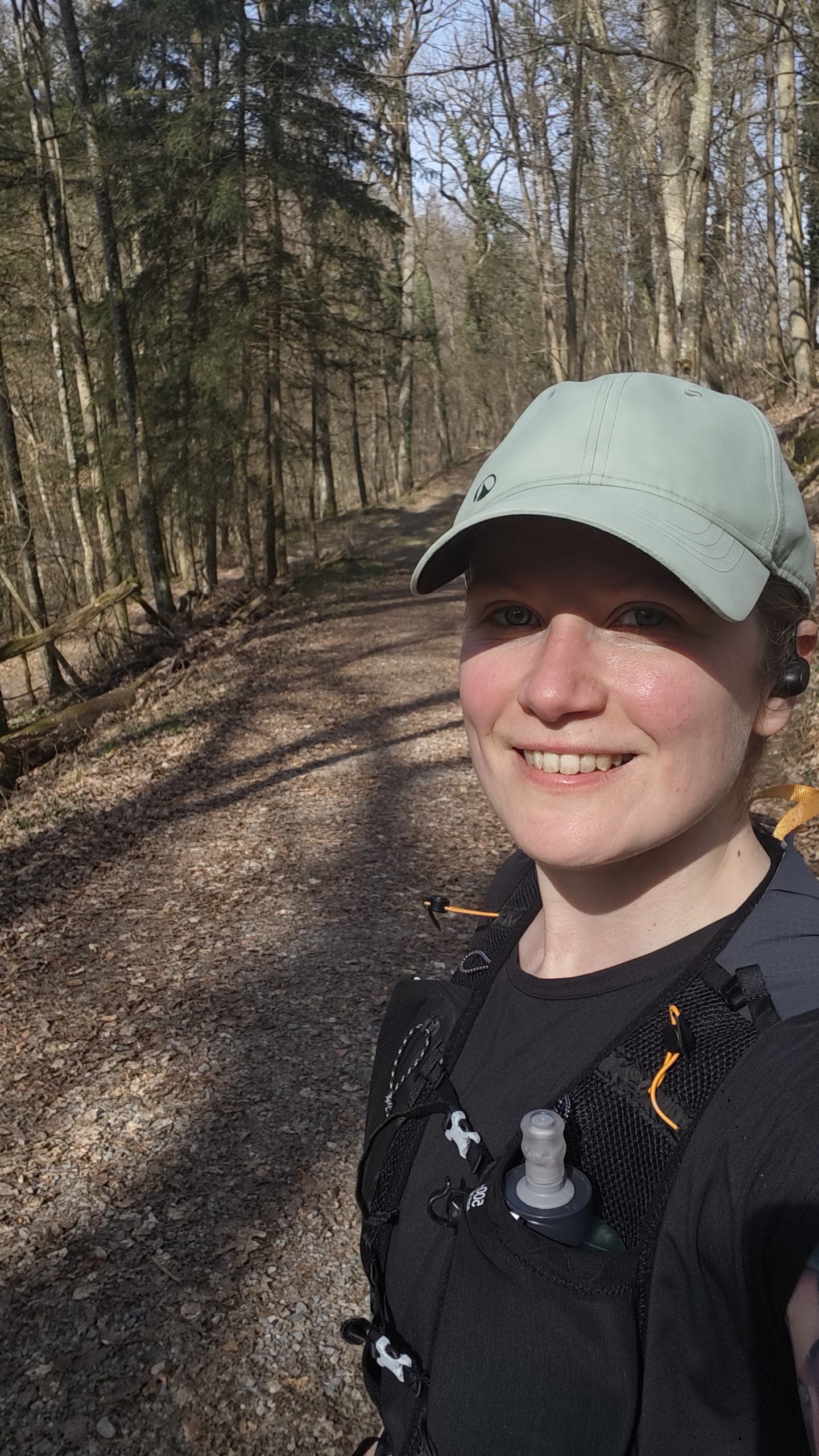 Eine Frau in einem Wald. Sie trägt Laufkleidung und ein Cap.